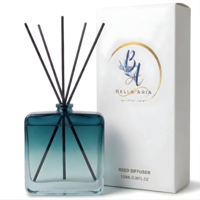 A square light blue glass reed diffuser bottle alongside its white packaging, and black reeds.