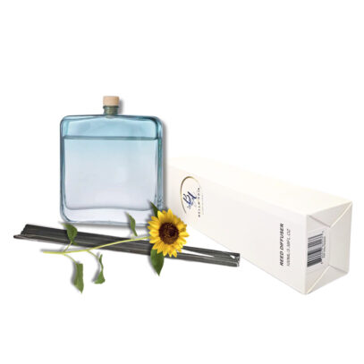 A square light blue glass reed diffuser bottle alongside its white packaging, black reeds, and a single sunflower.
